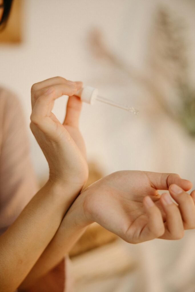 Close-up of hands using a dropper to apply skincare product.